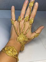 Gold-tone East Indian style hand jewelry shown worn on hand, connected from bracelet to five finger rings with detailed filigree and beadwork.