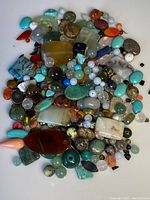 Wide view of assorted genuine loose gemstones and beads in various colors, shapes, and sizes on white background.