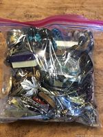 First plastic bag filled with assorted jewelry including metal bangles, beaded bracelets, silver-tone chains, and various pins and brooches in different colors and styles.