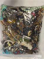 Photo of large sealed plastic bag of mixed jewelry from top angle showing variety of beads, chains, and jewelry pieces inside.