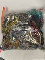 Photo of large sealed plastic bag filled with various mixed jewelry items including chain bracelets, beaded necklaces, and pendants.