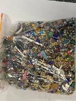 Photo showing large plastic zip bag filled with colorful mixed jewelry items including beads, chains, charms.