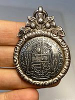 Front view of oval sterling silver fob pendant with engraved heraldic emblem and floral detail topper.