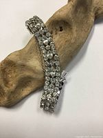 Three-row rhinestone bracelet laid on a wooden textured background, showing front view of stones.
