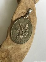 Closed front view showing oval sterling silver locket with raised floral design and bail for chain.