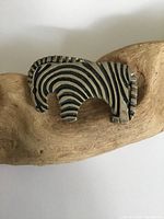 Front view of the sterling silver zebra-shaped brooch showing etched black stripes to represent the zebra pattern, resting on a piece of driftwood.