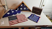 Four American flags including one in a framed triangular display case, and a black box containing the Pearl Harbor DVD gift set on a white table.