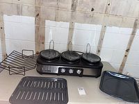 Overall view of the Bella 3-pot crockpot warming station with two oven trays beside it on table.