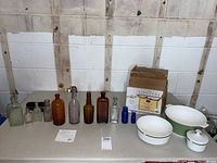Full view of all bottles, ceramic bowls, boxed photo frames on table against wall