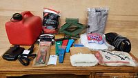 Photo of entire lot laying on wood surface including gas can, car jack, scrapers, cleaning cloths, polishing mitts, radar detector, and battery in packaging.