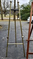 Photo showing gold-colored metal easel with adjustable height and locking knobs.