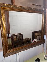 Full view of the large rectangular mirror with an ornate gold-toned frame and visible reflection of another room.