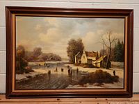 Full view of the framed oil painting showing house by river in winter with ice skaters.