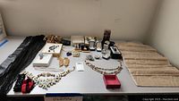 Wide view of various jewelry pieces and accessories laid on a table, showing necklaces, earrings, bracelets, a scarf, keychain, and rings.