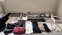 Full overview photo showing multiple pairs of gloves, scarves, and assorted accessories on a flat surface arranged in rows.