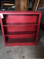 Full front view of the red painted bookshelf showing two movable shelves and scratches.