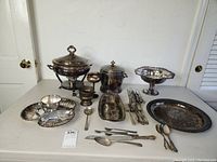 Overview of silverplate serving ware, multiple pieces arranged on table including trays, bowls, flatware and covered dishes