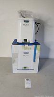 Front view of SoClean CPAP cleaner on top of its product box with plastic cover on tubing.