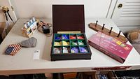 Photo showing the full wooden tea set open with 12 compartments containing various tea bags, Bigelow tea assortment box, wooden coat hanger with four pegs, cloth coasters with American flag and checkered designs, and a gourmet salt set with shaker bottles in a wooden rack.