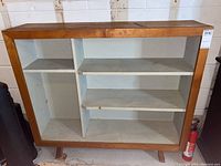 Front view of the wood bookcase showing multiple off-white painted shelves and compartments within a natural wood frame with angled legs.
