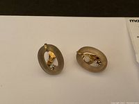 Front view of both earrings on white background showing frosted oval rings, gold settings, diamonds and beads