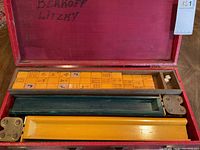 Red outer storage box open to show four wooden racks and a tray of yellow-orange mahjong tiles