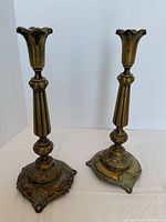 Pair of antique brass candlesticks standing side by side on white background, showing patina and detailed bases