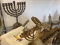 Multiple brass and silver-tone metal Hanukkah menorahs displayed on wire shelving