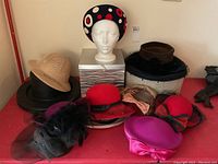 Group shot of all ten hats arranged on table with mannequin heads