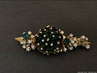 Flat-lay of gold-tone floral brooch showing emerald green glass beads and clear rhinestones