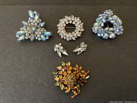 Five Sherman signed rhinestone jewelry items on black background showing brooches and earrings.