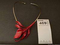 Full view of the necklace showing the red enamel flower pendant and gold-tone collar wire.