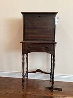 Front view of the vintage drop front cabinet with single drawer, showing the turned legs and pedestal base.