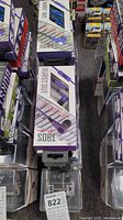 Multiple boxed Burst Out earbuds in purple packaging stacked on a shelf.