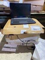 Samsung Chromebook 3 laptop on top of original cardboard box with visible product label and instruction manual on floor.