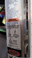 Close-up photo of ladder's side label showing usage modes and warnings in English and Spanish, including step ladder and scaffold uses.