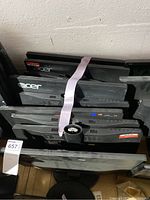 Top-down view of six stacked Acer monitors with model stickers and ports visible, showing condition and quantity.