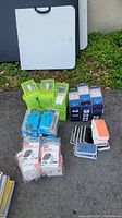 Wide angle photo showing all tech accessories including stacks of green fast USB chargers, blue earbud packages, and multiple Apple Watch cases in black, white, and orange.