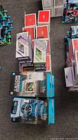 Stack of Owl Life and Burst Out mobile accessory boxes arranged on grey carpet. Includes car phone mounts, tablet holders, and earbuds.