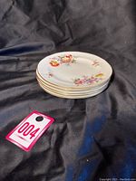 Stack of 5 antique Royal Crown Derby cake plates showing floral patterns and gold trim on a black background.