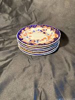 Stack of six Royal Crown Derby cake plates showing scalloped edges and thickness.