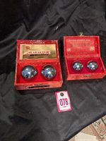 Two sets of polished iron healing balls displayed in red silk-lined boxes on a black fabric background, showing the size difference between the sets.