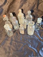 Full set of 10 vintage clear glass bottles in various shapes and sizes displayed on dark fabric background