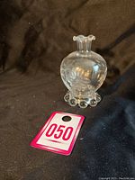 Front view of the small clear glass vase showing rounded body, ruffled rim, and beaded base with lot tag 050.