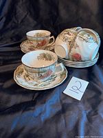 Set of six cups stacked and arranged with six matching saucers displaying the countryside village design and gold trim
