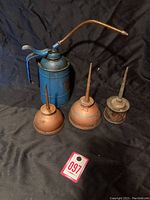 Full view of four oil cans: one large blue pump-style can and three smaller rust-colored cans with tapered spouts.
