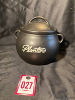 Front view of the black ceramic peanut jar with Planters logo and layered lid on black backdrop.