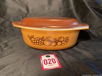 Side view of Pyrex casserole dish showing orange body with brown fruit pattern and brown lid.