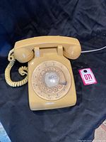 Front view of vintage mustard yellow rotary phone with dial and coiled cord