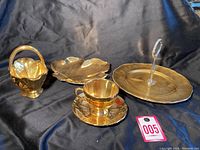 Front view of 5 gold-tone Royal Winton pieces on black cloth background showing tea cup with saucer, basket, leaf dish, and two-tiered serving tray.